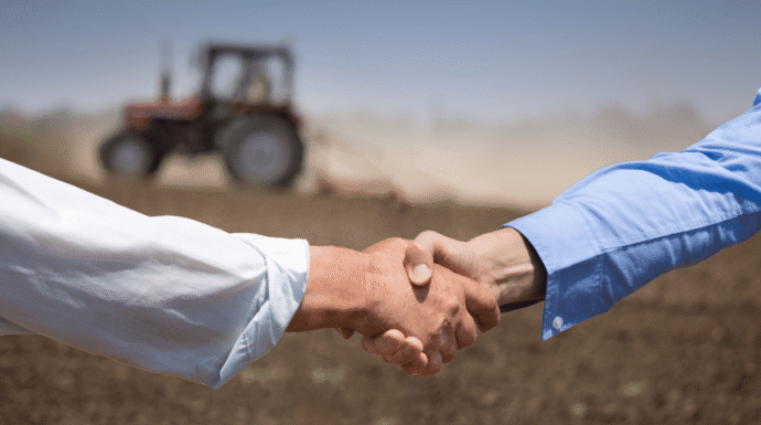 Two people shaking hands with a tractor in the back