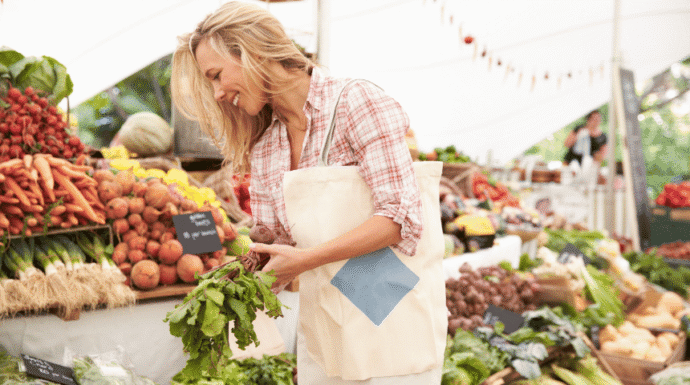 Farmer arranging fresh leafy greens at a farmers market, surrounded by colorful locally grown vegetables and produce.
